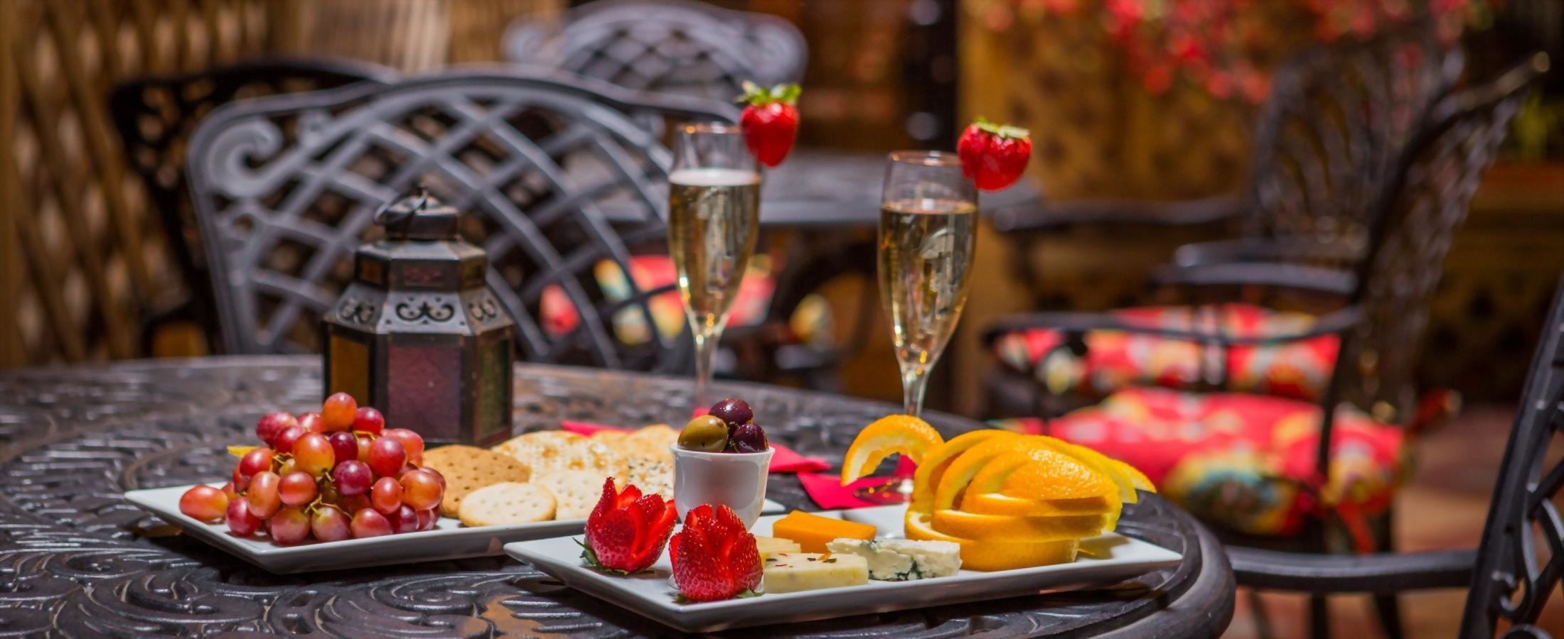 A table set with champagne, fruit, cheese, and crackers on a patio.