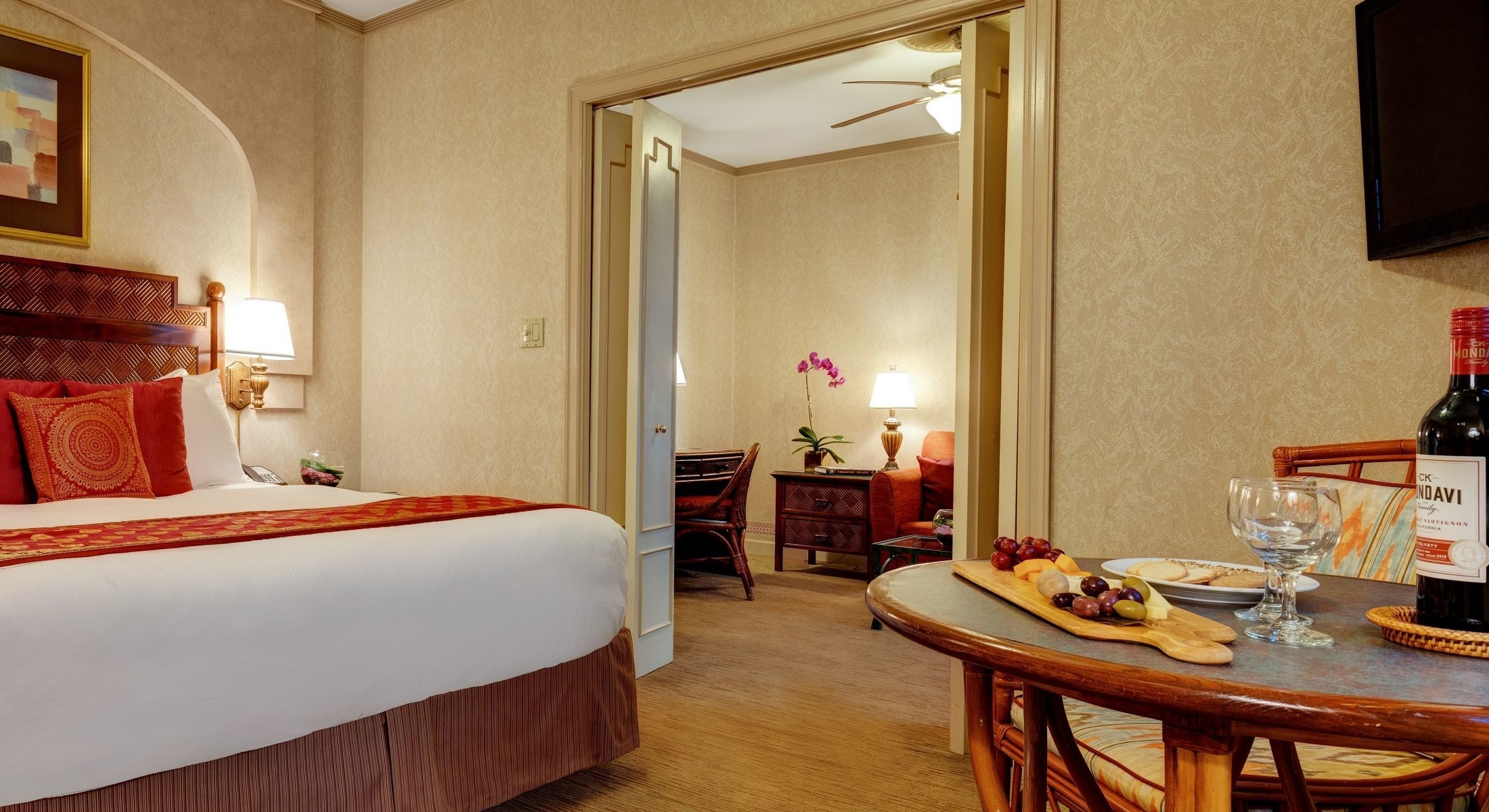 A hotel room with a bed, table, chairs, and a doorway to another room.